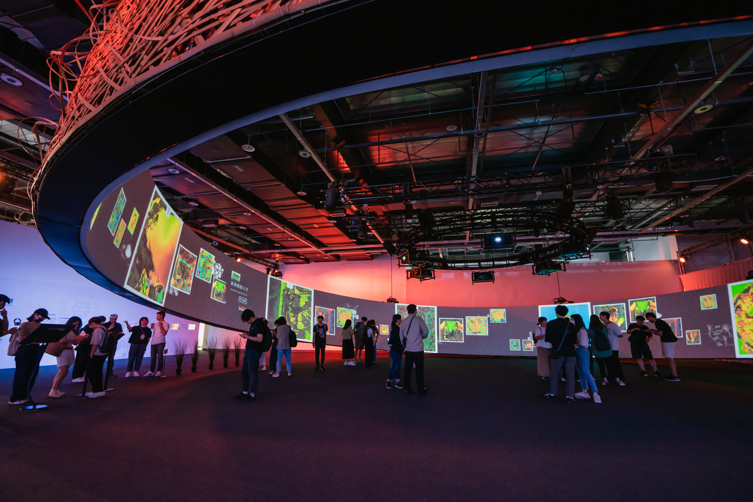 The suspended ring at the pavilion entrance, panels hanging from it under warm red light.