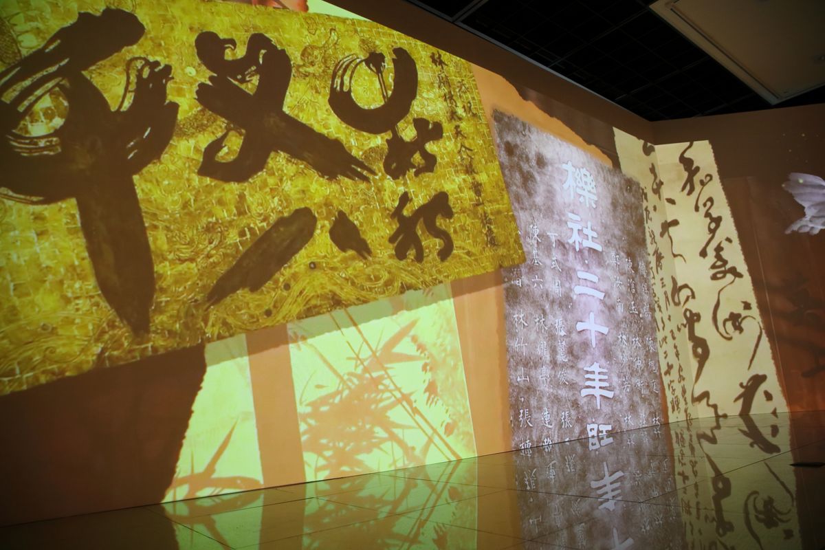 A gold calligraphy plaque and a weathered stone rubbing projected large on the wall, photographed objects set against a drawn interior.