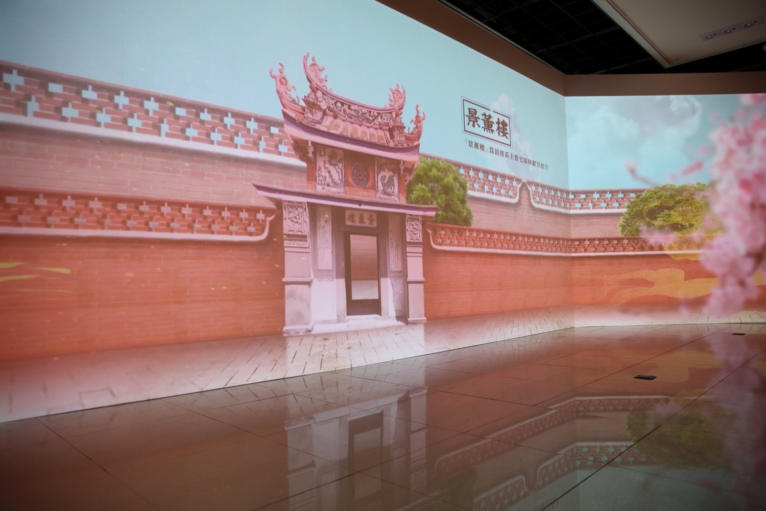 The projected courtyard wall running into the corner of the room and continuing onto the side wall, the brickwork mirrored in the polished floor.